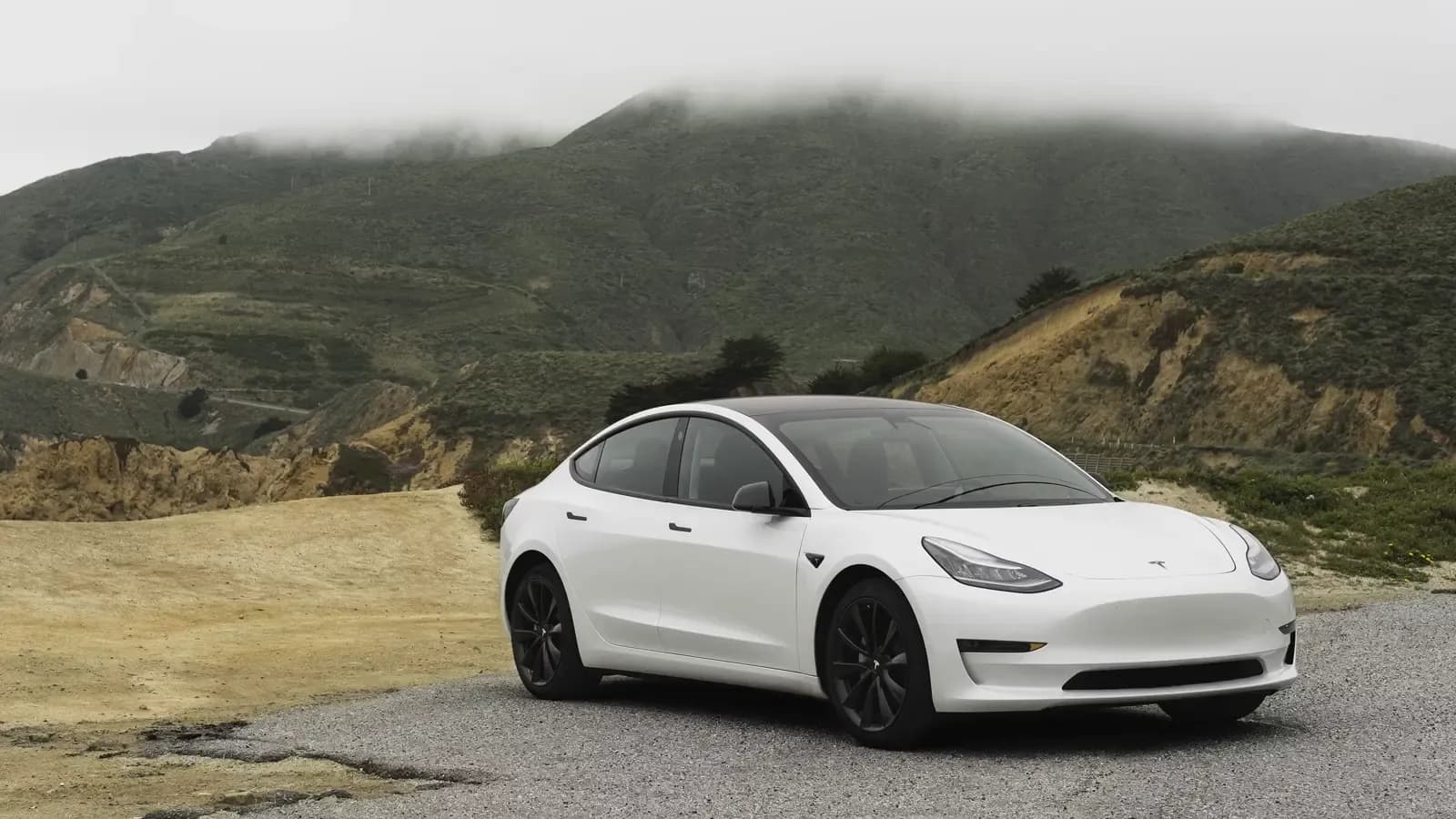 White Tesla Model 3 parked by a mountainous terrain